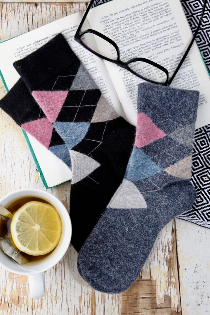Patterned angora wool socks beside an open book, glasses, and a cup of tea create a cozy reading scene.